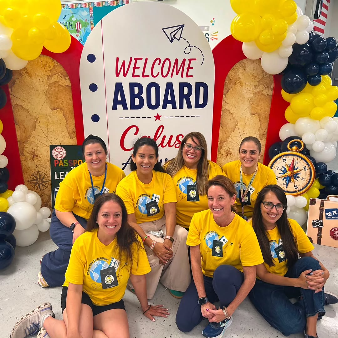The seven Calusa PTA board members in gold Passport to Learning shirts in front of the Welcome Aboard arch